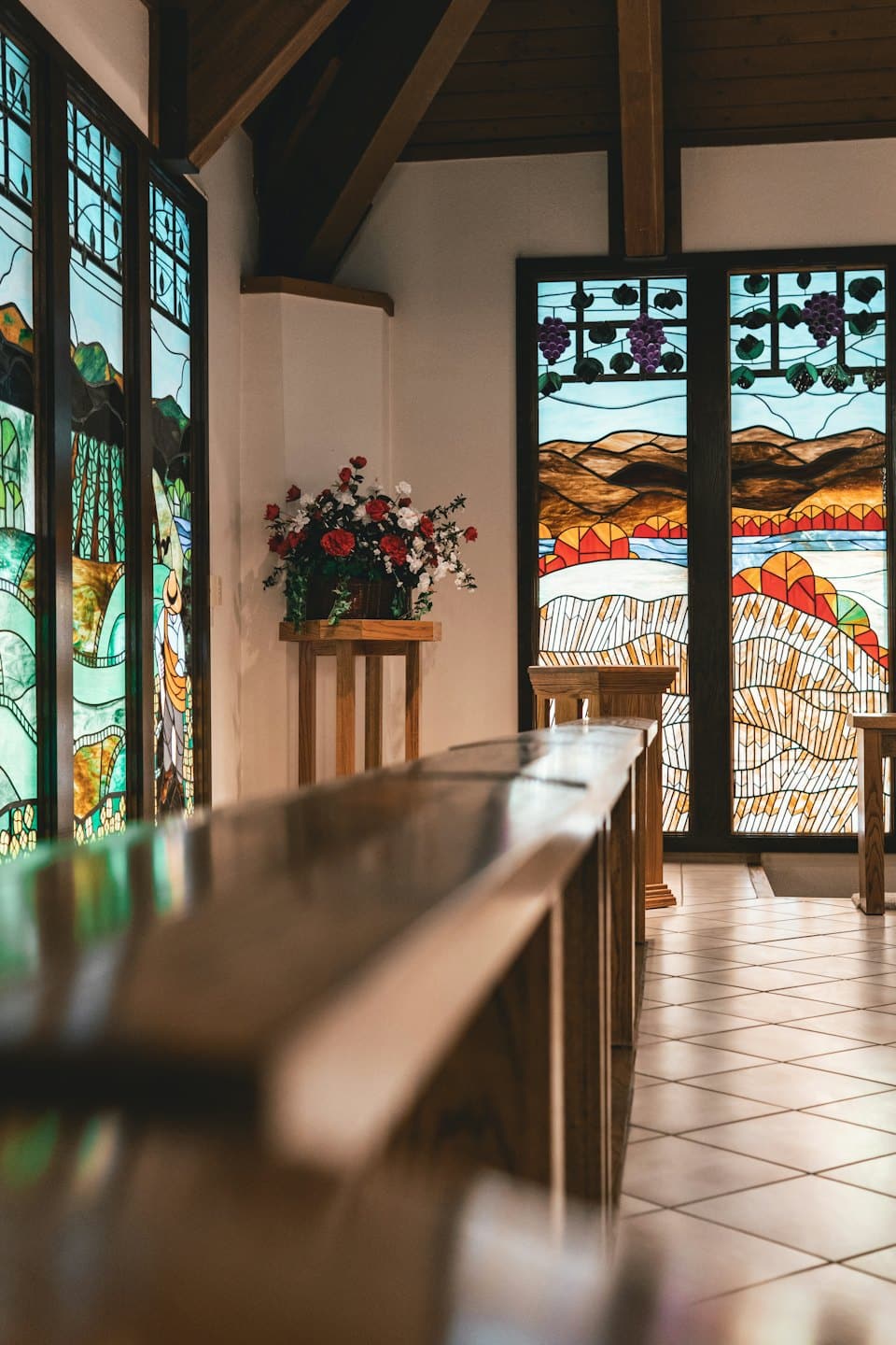 Kapel met glas-in-loodramen en bloemstuk op een standaard.