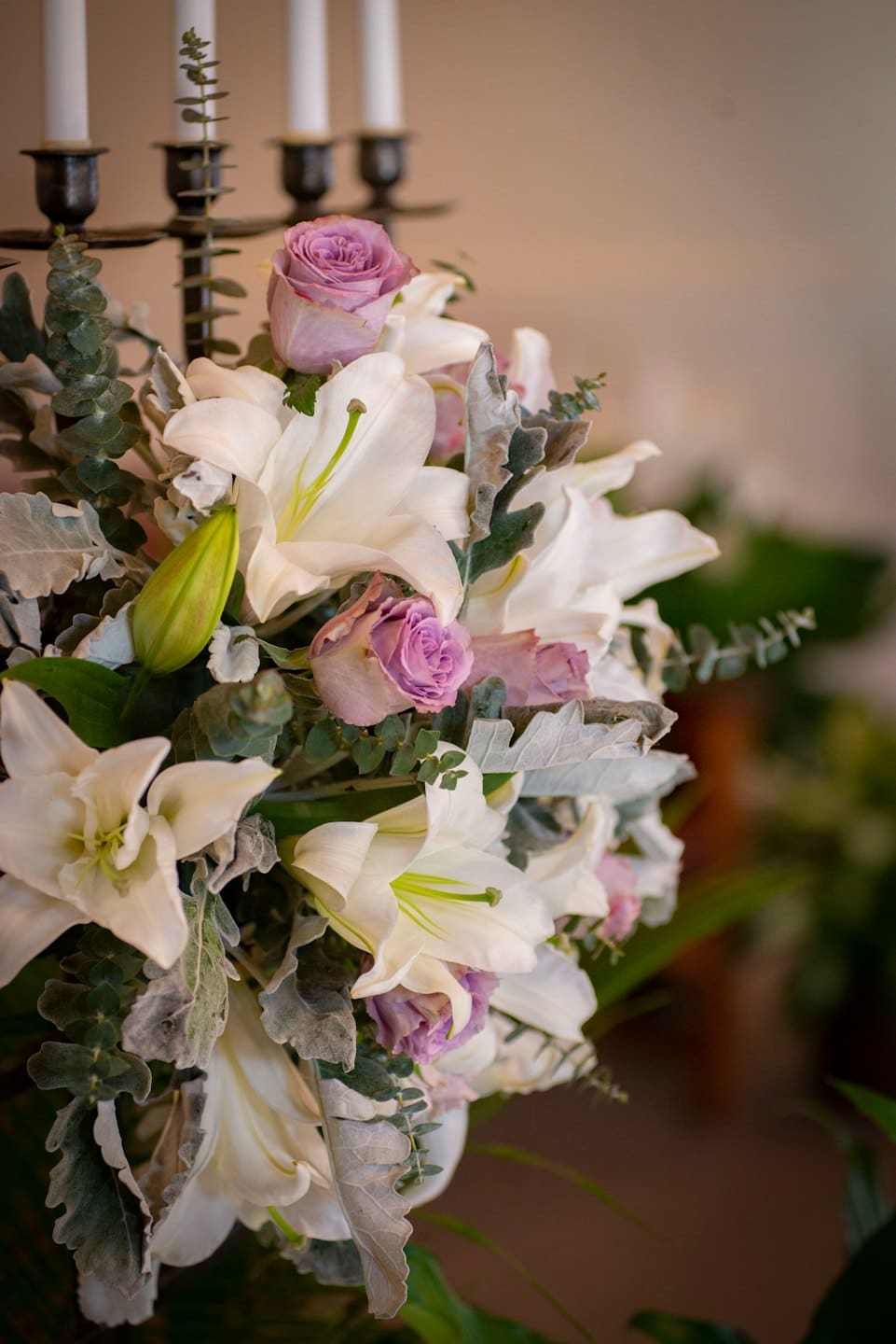 Witte lelies en paarse rozen gerangschikt met stoffige millerbladeren.